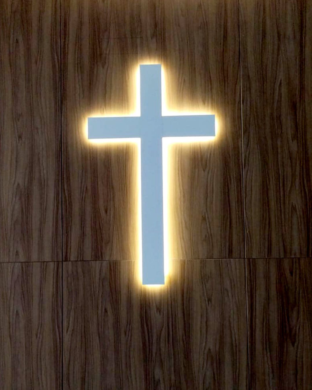 Cruz iluminada por LED indireto numa parede de madeira